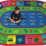 A child sitting on an educational rug with spanish and english words, letters and numbers