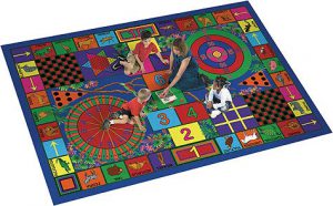 A woman and two kids siting on a large play rug with many games.