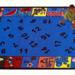 A child sitting on an educational kids rug with numbers in the middle and matching colorful objects around the edge of the rug.