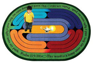 A child standing on a faith based rug that contains a maze and scripture from the bible.