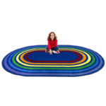 A child sitting on an oval kids rug with rainbow colored rings around the rug.