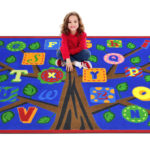 a child sitting on an educational kids rug with a tree and alphabet leaves.