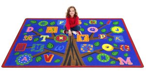 a child sitting on a blue kids rug containing the alphabet as leaves on a tree.
