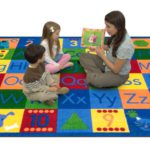 A teacher and children sitting on a classroom alphabet rug reading a book.