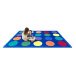 A woman and child sitting on a classroom seating rug with circles displayed on the rug.