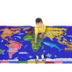 A child sitting on a classroom rug containing a map of the world.